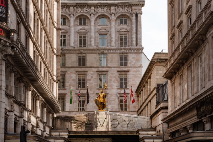 The Savoy Hotel in London with its entrance, golden statue, and international flags.